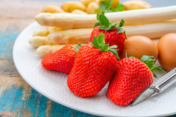 Spring in Netherlands, high quality Dutch white asparagus, washed and peeled on board with fresh red ripe strawberry