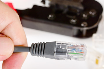 Engineer's hand holds patch cord with RJ45 connector and crimping tool for home Internet...