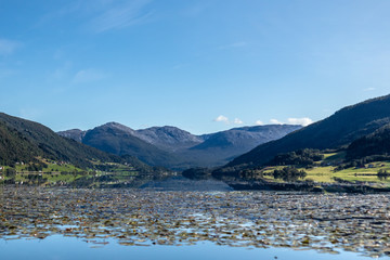 Norway mountains lake mirror on sunny day landscape. Hills reflection on water surface, blue sky, bright colors 
