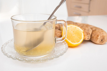 Glass cup of hot ginger tea with ginger rhizome (root) sliced and lemon, isolated on white background.