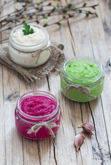 Russian appetizer horseradish with beetroot, green horseradish wasabi, white horseradish with lemon in jars on a linen napkin on a light wooden background in rustic style
