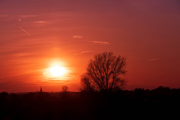 Imposanter Sonnenuntergang hinter einem Kirchturm und einem Baum