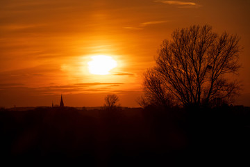 Imposanter Sonnenuntergang hinter einem Kirchturm und einem Baum