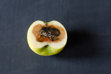 Cut rotten apple on a dark wooden background. Copy space, horizontal orientation.