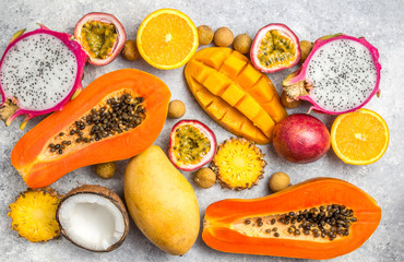 Set of exotic tropical fruits on light gray background - papaya, mango, pineapple, dragon fruit, orange, coconut, passion fruit, longan. Top view