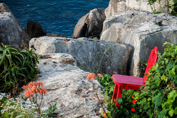 lonely red chair, on the edge of a cliff, on the stones and green of nature, facing the sea or the ocean