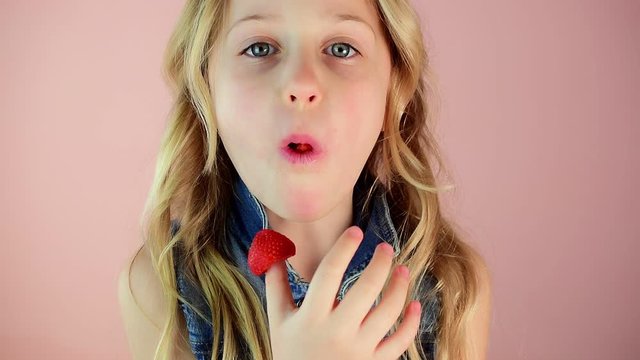 Cute little girl with blond hair eats tasty ripe strawberries