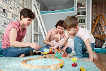 A young gay lesbian family with two children, a son and a daughter, spend time at home. They sit on the floor and play with children's toys.