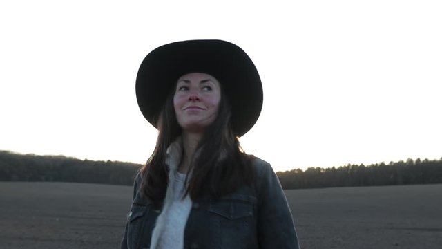 Cowgirl or cowboy girl walking on empty field at sunset wearing cawboy hat. 4K