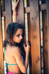 Fototapeta na wymiar Portrait of a beautiful young girl in blue swimsuit leaned against a wooden fence.