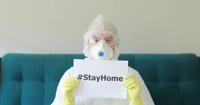 Portrait of doctor man in protective suit, respirator, glasses with inscription hashtag stay at home. Call for quarantine, isolation. Coronavirus pandemic, epidemic. Stayhome to fight with COVID-19.