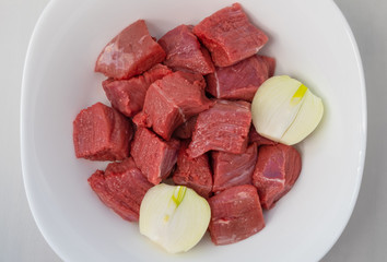 Fresh beef fillet cut into pieces, and onions in a white bowl. Horizontal orientation, selective focus. Top view.