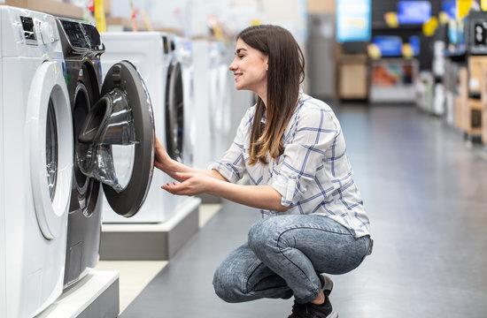 A young woman in a store chooses a washing machine.