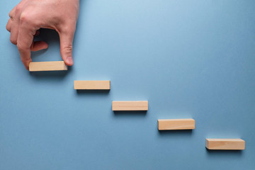 Concept of business development stages. Hand holds wooden blocks on a blue background.