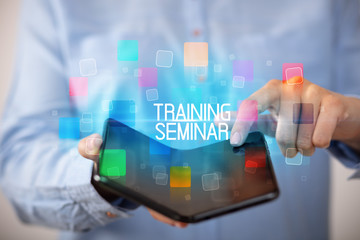 Young man holding a foldable smartphone with TRAINING SEMINAR inscription, educational concept