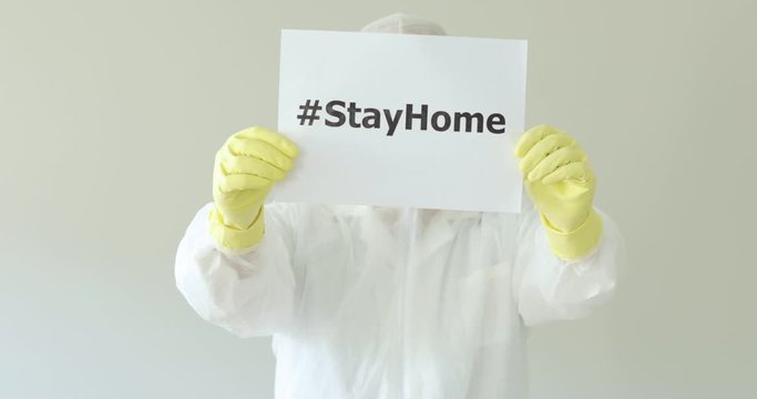 Portrait of doctor in protective suit holding inscription hashtag stay at home on white background. Call for quarantine, isolation. Coronavirus pandemic, epidemic. Stayhome to fight with COVID-19.