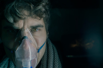 Dark Portrait of man using steam vapor inhaler nebulizer doing aerosol inhalation medicine...