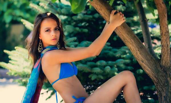 teen girl hanging on a tree like a monkey. Brunette with long hair hanging on a branch. Young attractive girl in a swimsuit in warm summer day. Travel, adventure, photo shoots in hot countries.