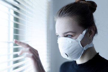 young woman with green eyes and with black shirt and ffp3 protective mask at the window