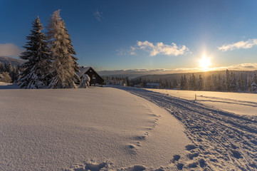 Zasypana śniegiem droga prowadząca do chaty w czasie zachodu słońca
