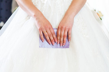 The bride holds a purple envelope in her hands, a French manicure