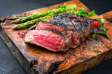 Gegrilltes dry aged Wagyu Entrecote Beefsteak mit grünen Spargel und Salat als closeup auf einem...