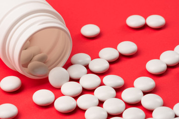 A handful of white tablets or vitamins or food additives poured out of a white bubble on a red uniform background.