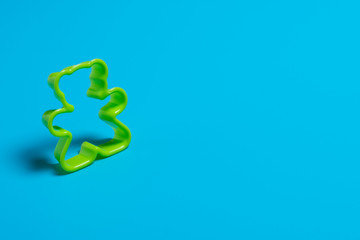 Green plastic cookie cutter for making cookies in the shape of a teddy bear on a blue background....