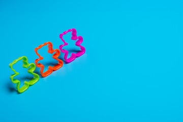 Three multi-colored plastic cookie cutter for making cookies in the shape of a teddy bear on a blue background. Culinary concept. Flat lay with copyspace.
