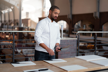 Handsome young chef African ethnicity lays knives on table in front of a culinary master class.