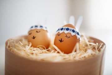Two little easter eggs with a painted drawn rabbit faces and ears on them laying in hay on the table isolated. Easter holidays decorations and preparations concept. Holy religious day. Copyspace.