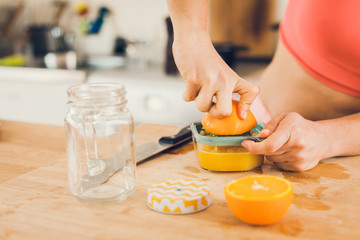 Young woman in sportswear squeezing oranges on a table, preparing juice.