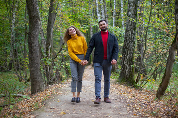 Fototapeta premium Guy and girl hold hands walk down the track looking into a camera in the park