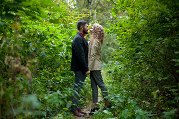 Girl and guy hold hands looking at each other among green bushes in park
