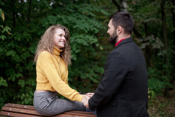 Young man and girl sit on back of bench for sitting hold hands smile to each other