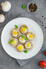 Stuffed mushrooms with quail eggs on a white plate with basil and thyme leaves on a dark concrete background. Easter appetizer. Vertical orientation. Top view.