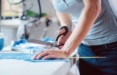 Woman cutting fabric with tailor scissors on tailor’s table