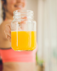 Young woman in sportswear holding a jar of freshly squeezed orange juice at home.
