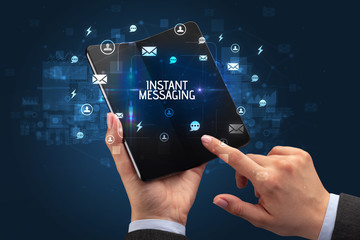 Businessman holding a foldable smartphone with INSTANT MESSAGING inscription, social networking concept