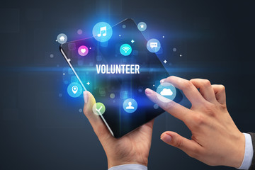 Businessman holding a foldable smartphone with VOLUNTEER inscription, social media concept