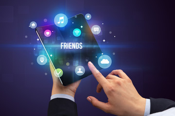Businessman holding a foldable smartphone with FRIENDS inscription, social media concept