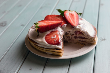Pancake pie with strawberries. Dessert with cream and berries. National cuisine. Sweet pastries on a wooden table. Background of turquoise boards.