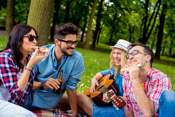 Friends in park enjoying time together, playing guitar, eating pizza and drinking beer