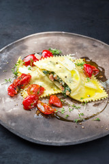 Traditionelle italienische Pasta Ravioli angeboten mit Lachs Spinat Füllung und gebratenen Tomaten als closeup auf einem rustikalen Modern Design Teller