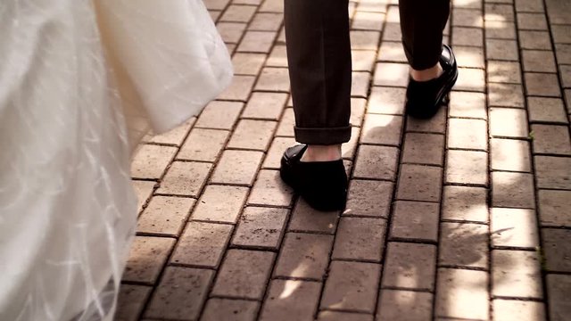 Caucasian couple, man in moccasins and a girl in a white long dress walk along the path with stones. Legs back to knees close up