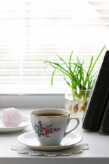 Tea in a vintage cup, marshmallows on a vintage saucer and old books on a light background.