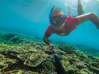 Selfie of man snorkeling on a beautiful healthy coral reef garden, with an action camera, in pristine blue water. A bearded man diving through the colorful coral in Raja Ampat, Indonesia.