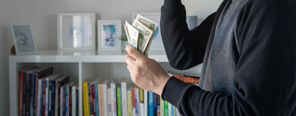 Side view of unknown caucasian man midsection holding american dollars USD and Euro EUR banknotes money in hand at home in day