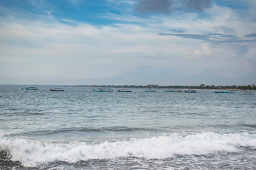 A beautiful cloudscape day beside the seashore with the silhouette of horizon mountain and floating boats in Kuta, Bali
