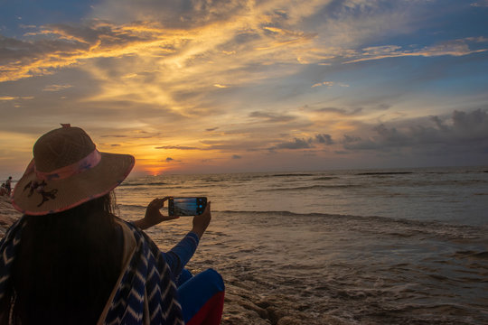 Woman tourist trying to take the picture of beautiful sunset through the horizon from the seashore in Bali